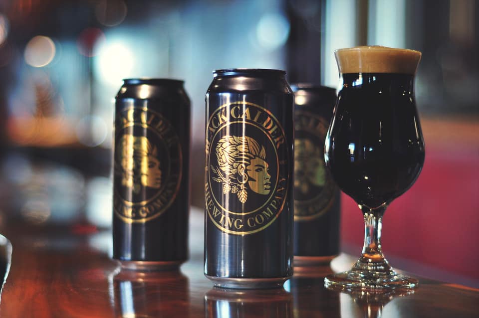 black calder logo design on cans next to glass of beer